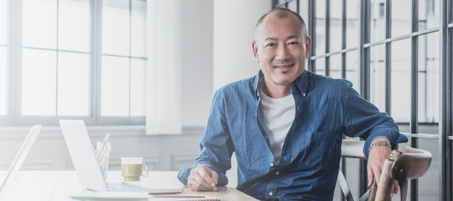 Man in casual attire sits with his laptop and mug.